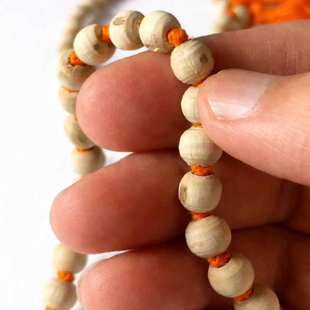 A handcrafted natural Tulsi Mala made from authentic light-brown basil wood beads, strung together with a traditional orange tassel. The beads show natural wood grain textures, symbolizing purity and devotion.
