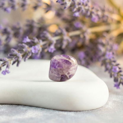 Polished Amethyst tumble stone placed on a white surface, known for calmness, intuition, and spiritual protection.